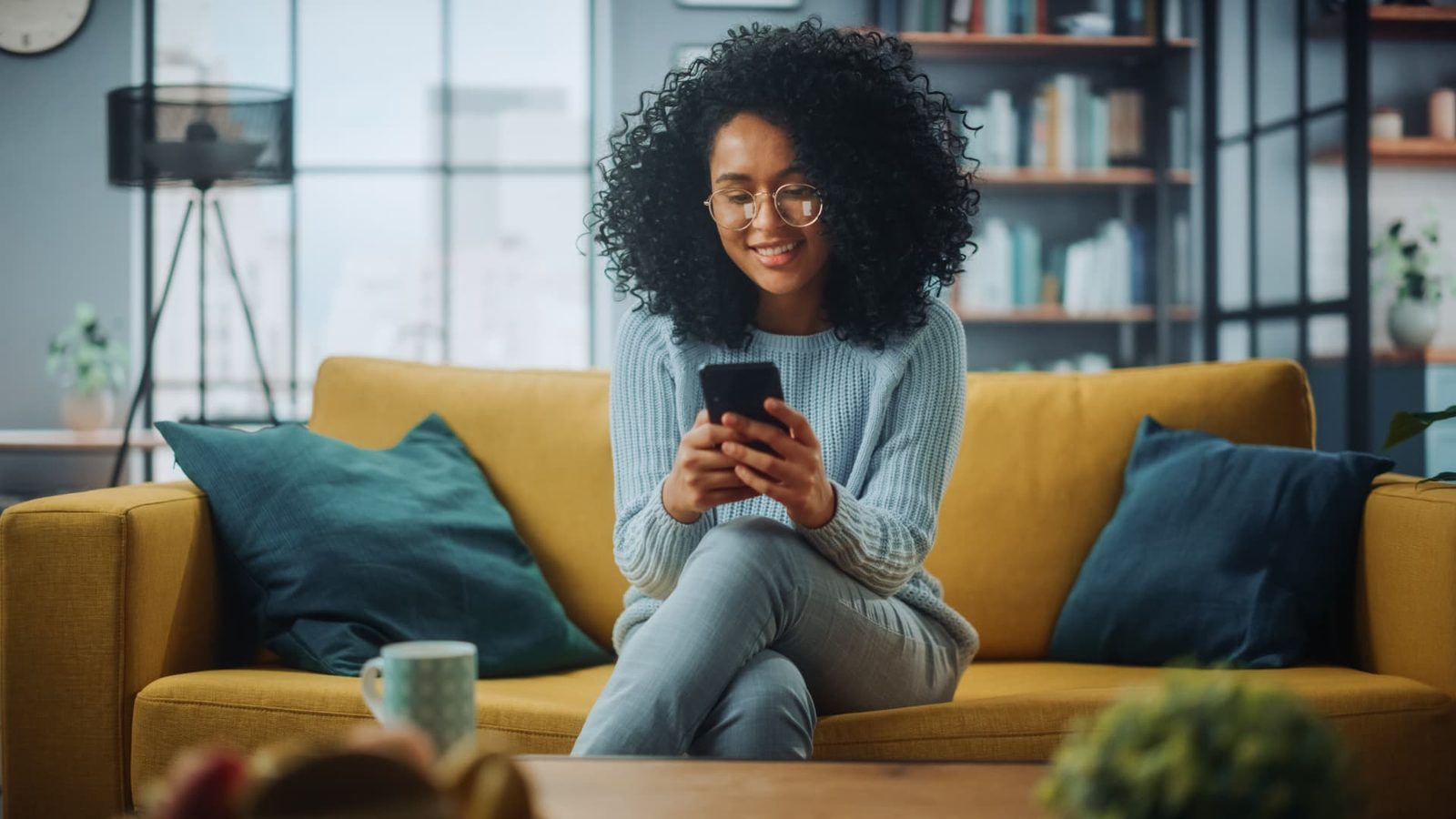 A person sitting on a yellow sofa, smiling while reading an answer on a smartphone