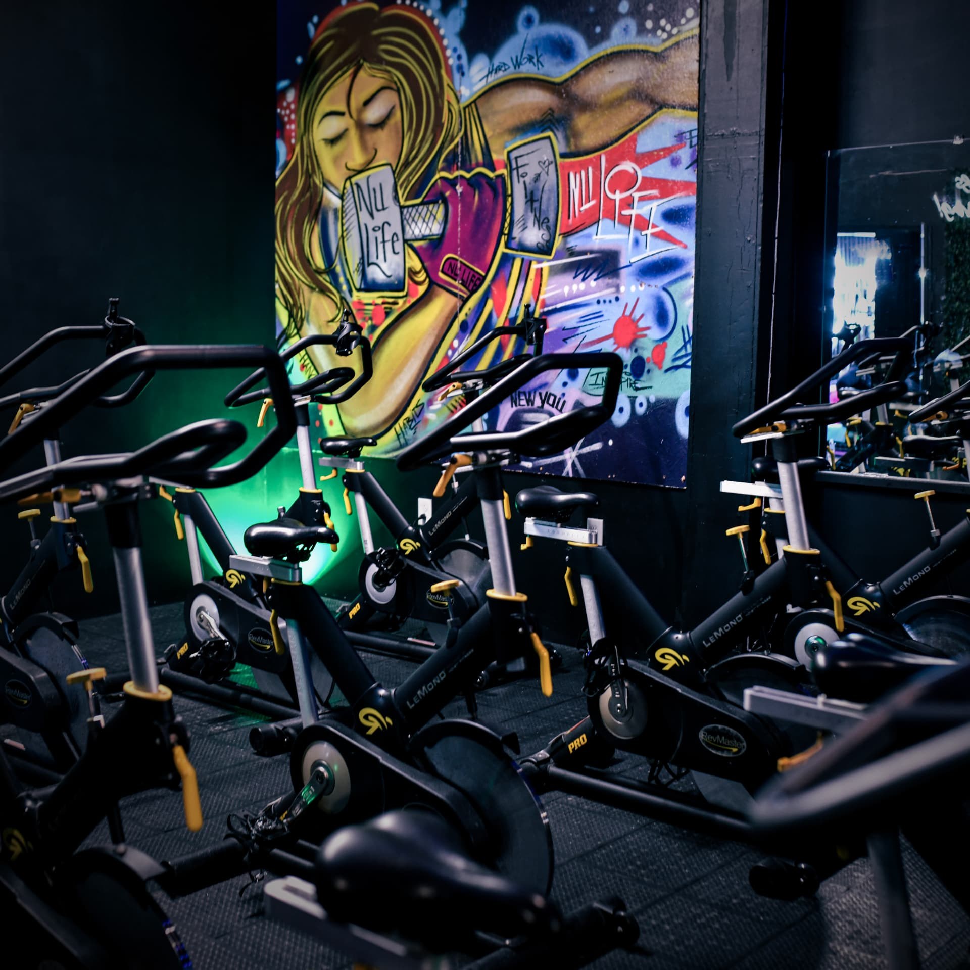 Indoor cycling bikes in front of NuLife's colorful studio mural