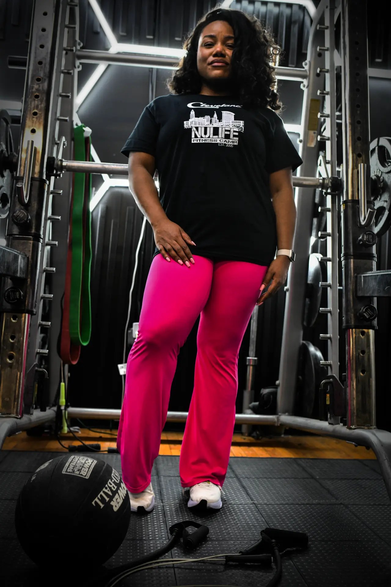NuLife trainer in bright pink leggings standing beside a medicine ball